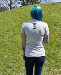 Female model wearing a cream colored t-shirt with a small, No Egrets birdcage logo in black on the back between the shoulders.