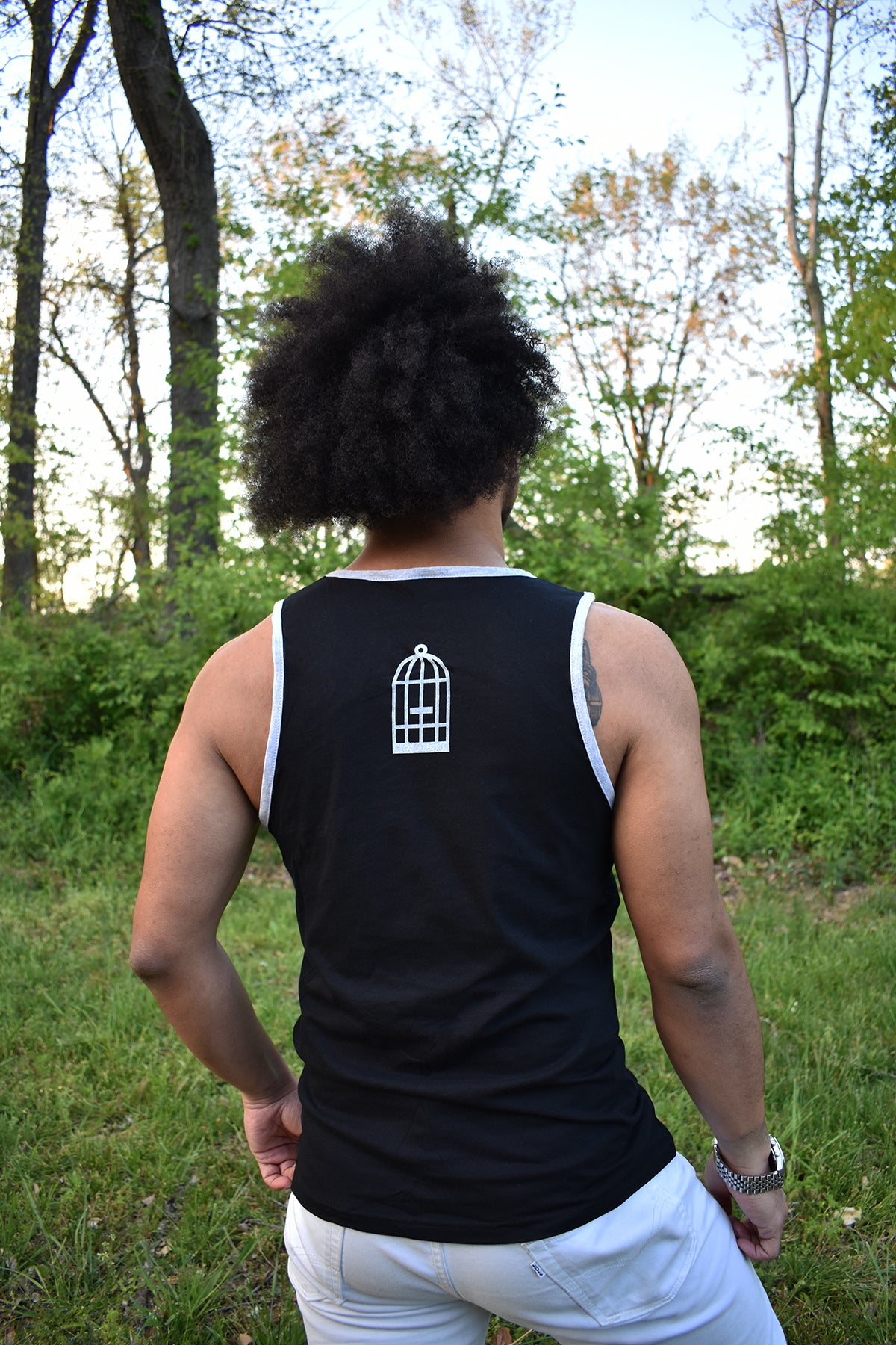 Male model wearing a black and grey ringer tank top with a small No Egret's birdcage logo in grey on the back between the shoulders.
