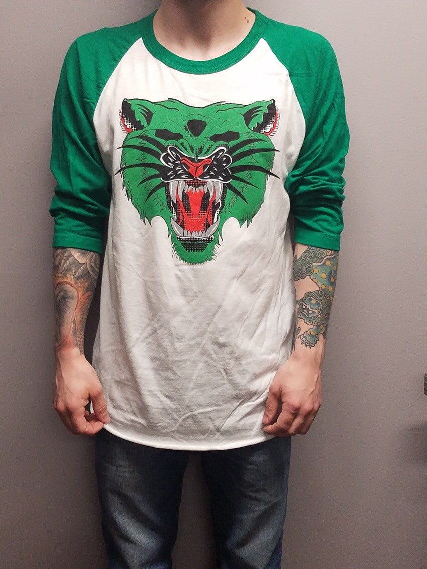 Male model wearing a baseball tee with a white body and green sleeves with Ben Drawdy's Battle Cat design in green, red, and black on the front.